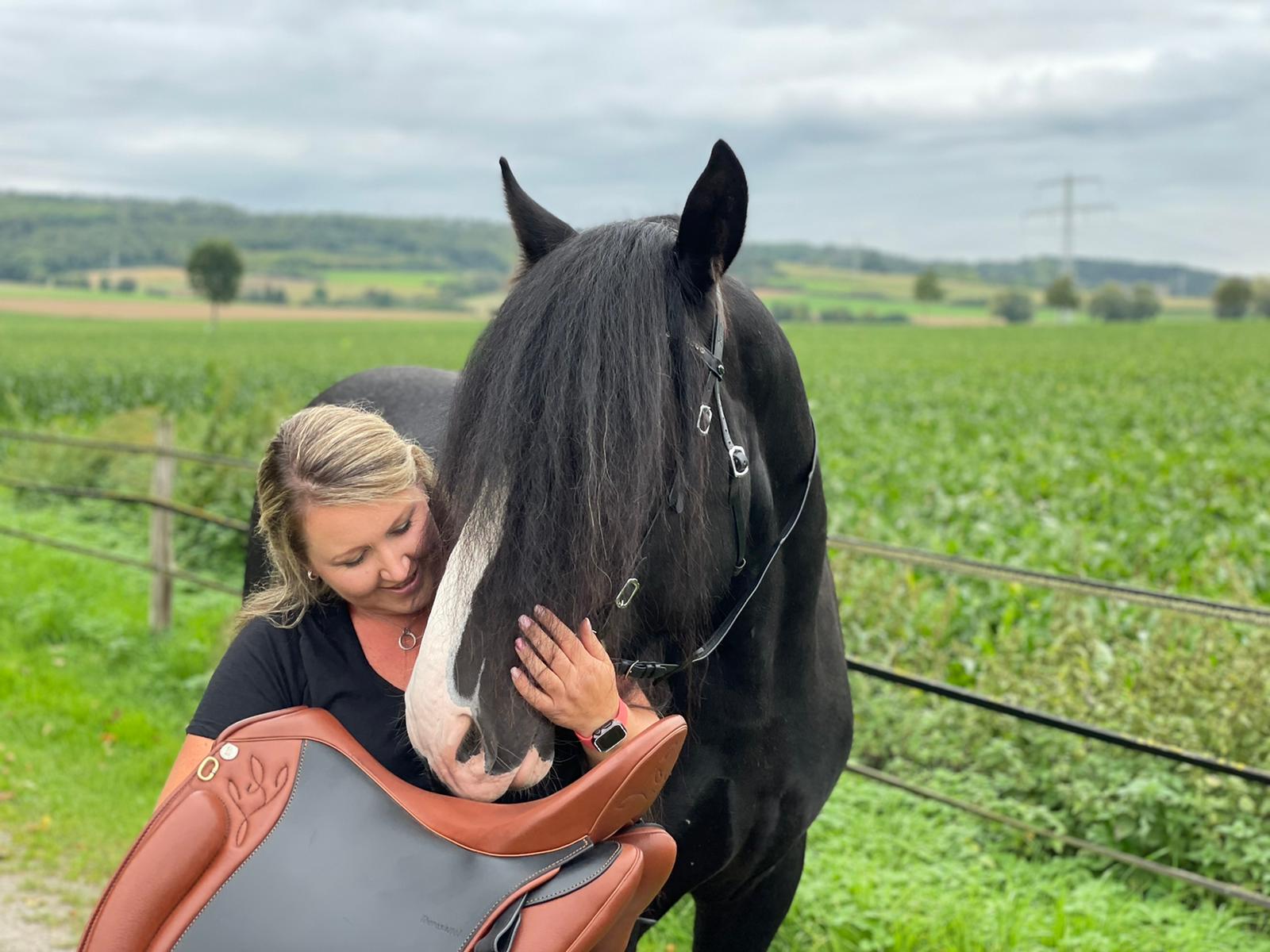 Carina mit einem schwarzen Pferd und einem Sattel auf der Weide